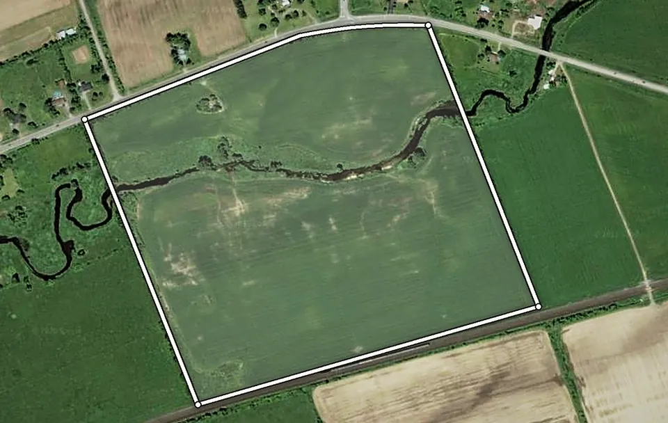 Satellite view of the 88.5-acre parcel outlined between County Road 1 and the CN rail line, bounded by a tree line on the west and the neighbouring field on the east, with the creek crossing it